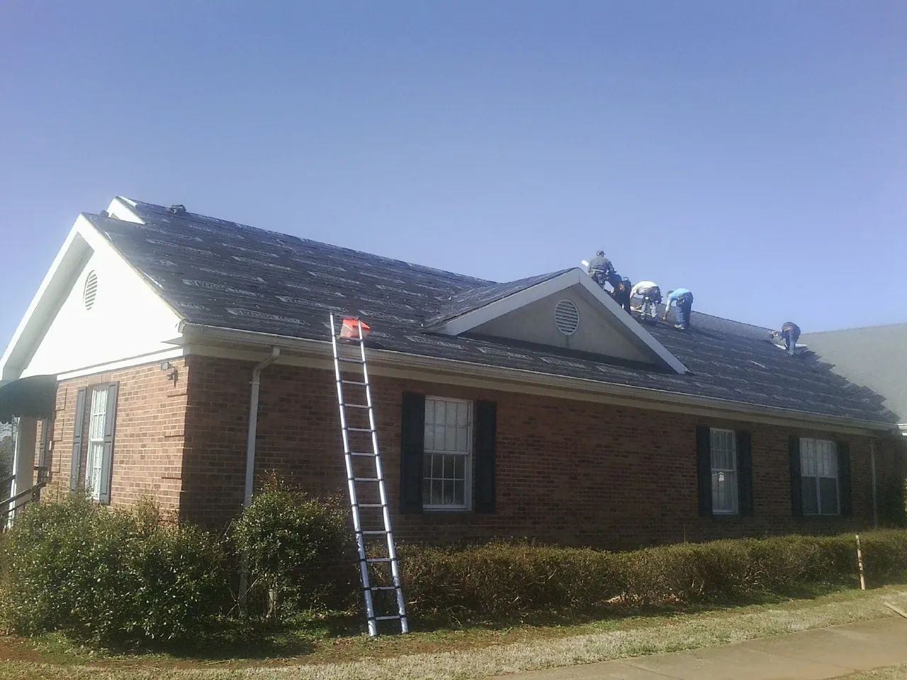 Crew tearing shingles off a brick ranch roof with a ladder set — Metal Roof Repair work by our crew in San Miguel