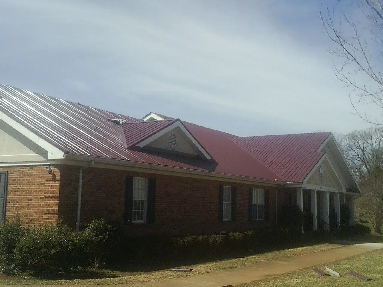 Red metal roof with gabled entries on a long brick building, from a Hail Damage Roof Repair job in San Miguel
