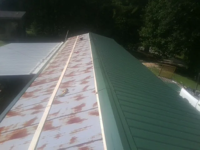 Old rusted panels beside newly installed green metal roofing — Wind Damage Roof Repair by Roofing Brothers in San Miguel