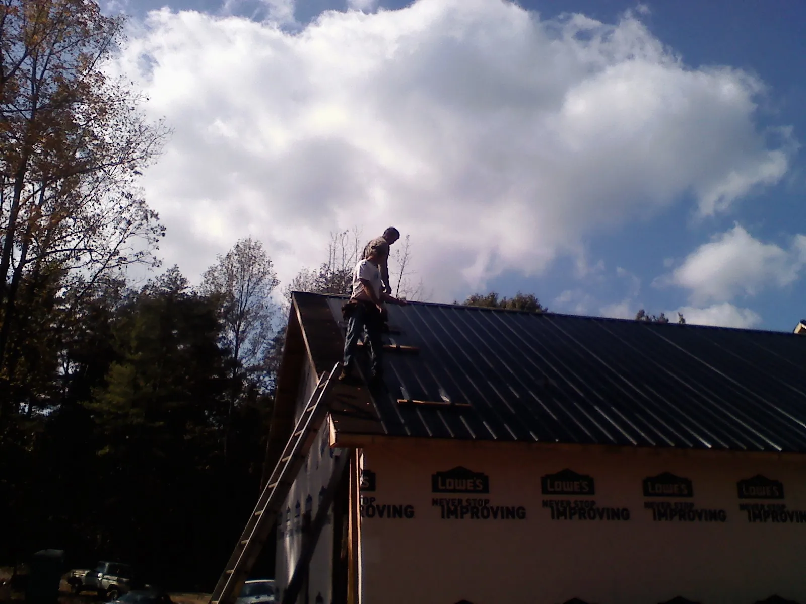 Roofer fastening dark metal panels high against a cloudy sky, from a Roof Inspection job in San Miguel