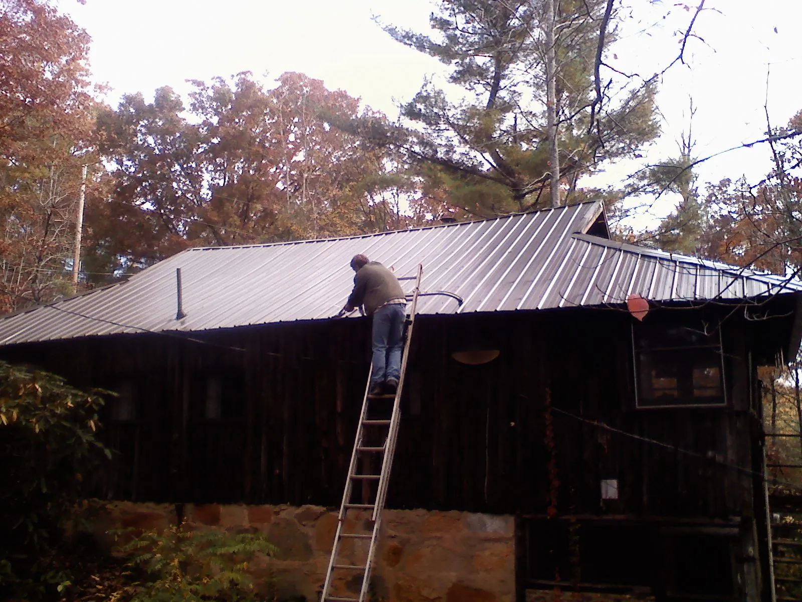 Roofer on a ladder working along the edge of a cabin metal roof in San Miguel
