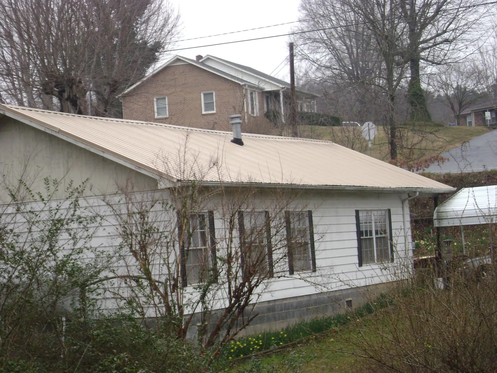 Tan metal roof on a white sided house set into a hillside — Commercial Roofing by Roofing Brothers in San Miguel