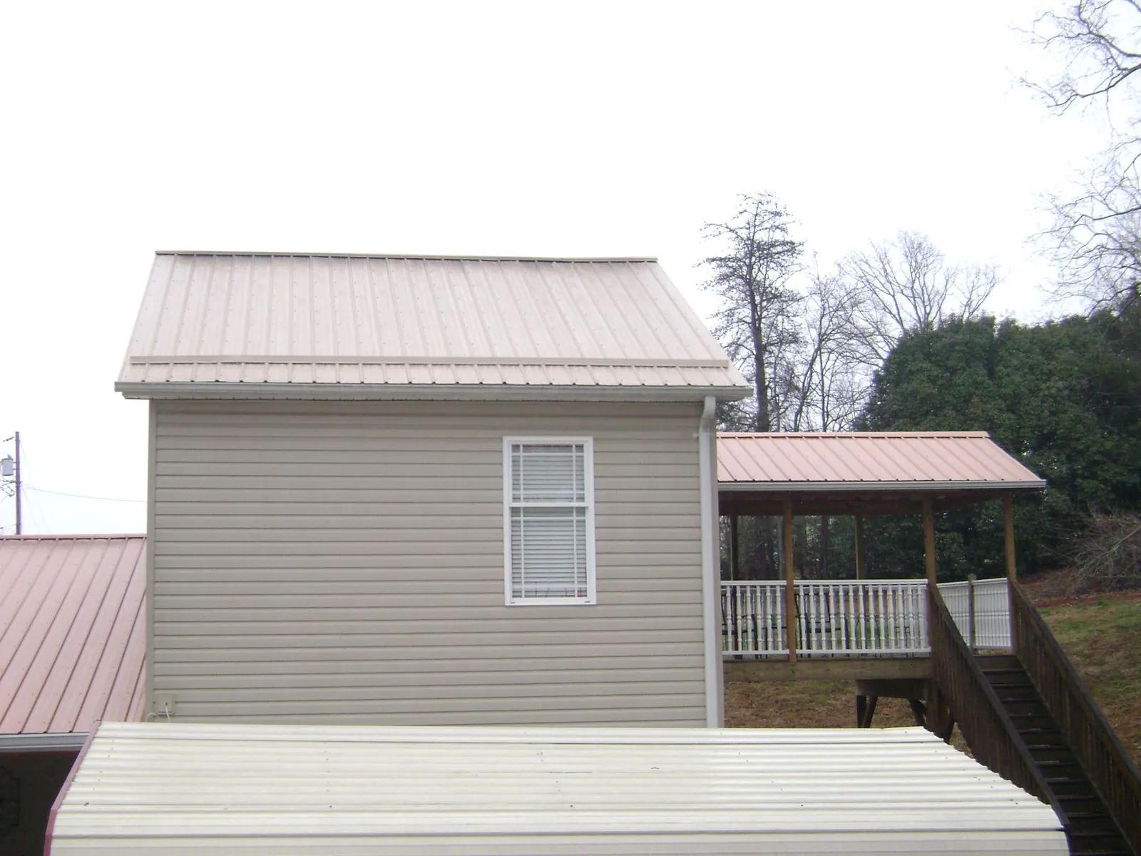 Tan metal roofs on a two story addition and attached porch, from a Roof Replacement job in San Miguel